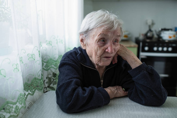 Uma mulher idosa sentada na cozinha de seu apartamento
. - Foto, Imagem