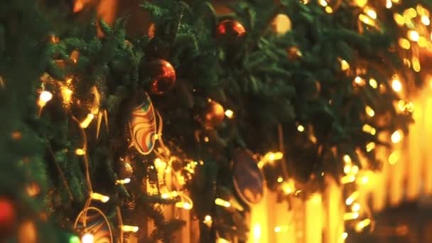 Kamerafahrt von unten nach oben mit Fokus auf farbige Kugeln, die an der mit wunderschönen Dekorationen und Mini-Lichtern bedeckten Weihnachtsbaumgirlande hängen. Festlicher Straßenschmuck in der europäischen Stadt - Filmmaterial, Video