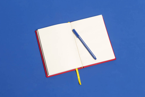 Cuaderno rojo abierto con cinta amarilla de separador sobre una mesa de color azul clásico y lapicero. Colores de la bandera de Colombia - Foto, Imagen