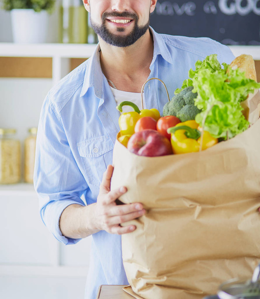 Man holding paper bag full of groceries on the kitchen background. Shopping and healthy food concept - 写真・画像