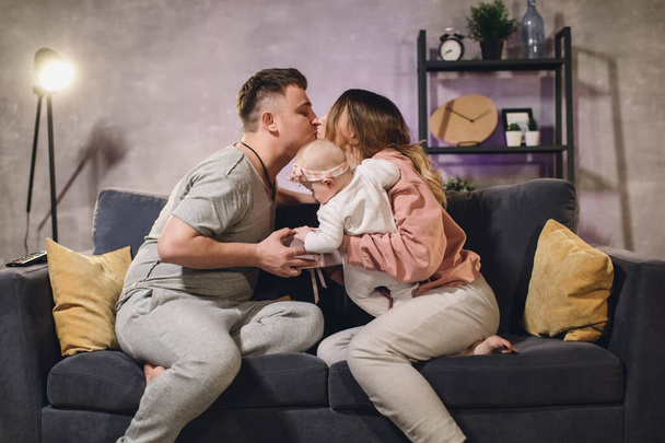 Young family in a cozy apartment on the couch. The family is happy. The husband gives a gift to his wife. - Zdjęcie, obraz