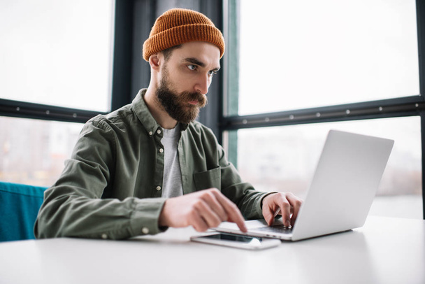 Laptop kullanan yakışıklı sakallı adam, ofisinde oturuyor. Genç düşünceli metin yazarının portresi klavyede daktilo ediyor, evden çalışıyor. Üniversite öğrencisi, çevrimiçi eğitim kavramı - Fotoğraf, Görsel