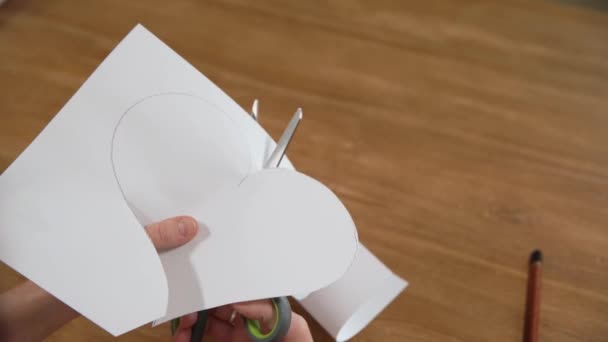 una mujer joven dibuja un corazón en un papel blanco y luego lo corta con tijeras. Producción de regalos por amor
 - Metraje, vídeo
