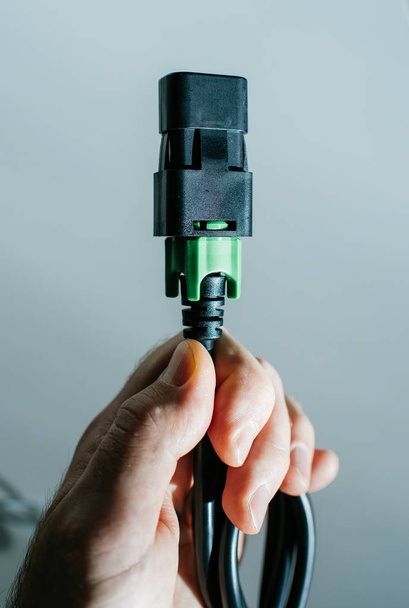 Man hand holding black and green IEC power cable against blue - Fotoğraf, Görsel