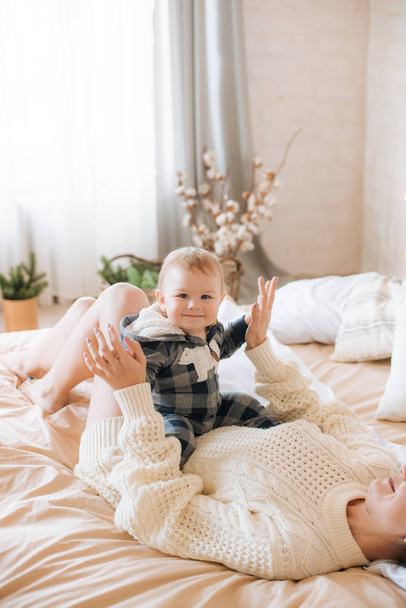 Young mother and little toddler son in a Scandinavian style bedroom decorated with Christmas garlands and needles on a large bright bed. Christmas mood - Fotografie, Obrázek