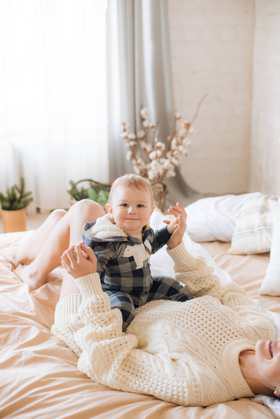 Young mother and little toddler son in a Scandinavian style bedroom decorated with Christmas garlands and needles on a large bright bed. Christmas mood - Фото, зображення