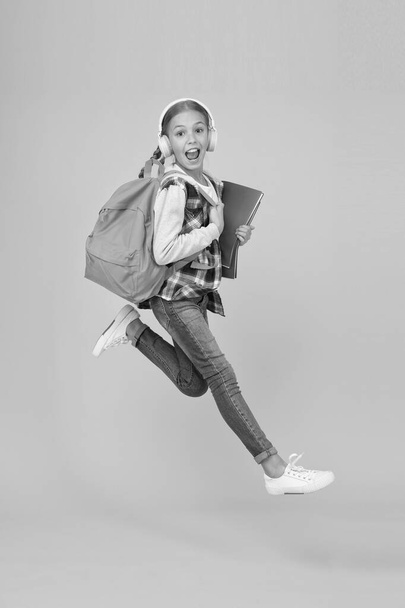 Getting back into studying. Energetic little girl run to school yellow background. Small child with school bag and books back to class. Back to school time. Happy welcome back - 写真・画像