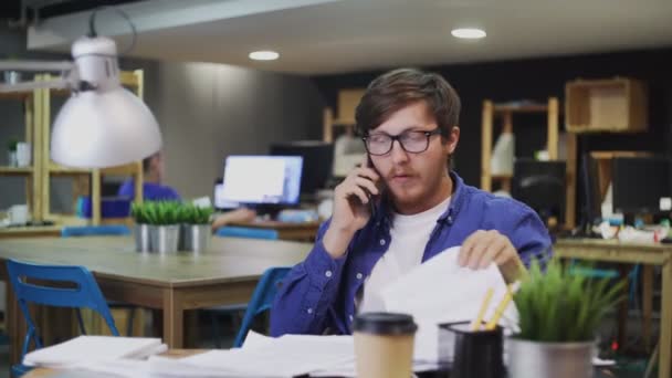 Νεαρός επιχειρηματίας μιλάει στο κινητό τηλέφωνο amd έλεγχο των οικονομικών καταστάσεων στο γραφείο - Πλάνα, βίντεο