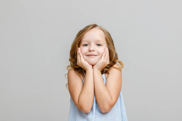 Portret van een schattig klein blond kind meisje op een grijze achtergrond - Foto, afbeelding