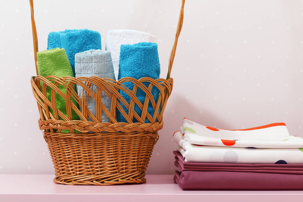 On the dresser there is a stack of clean ironed bed linen and there is a basket in rolls of folded multicolored towels - Foto, Bild