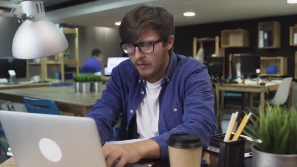 Bosszús programozó szemüveggel dolgozik laptop az irodában - Felvétel, videó