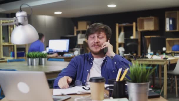 Happy Young Man rozmawia przez telefon siedząc w biurze. - Materiał filmowy, wideo