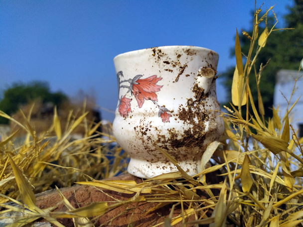 una taza de té de arcilla blanca con suciedad puesta sobre una hierba amarilla seca
 - Foto, Imagen