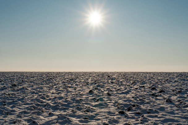 Τοπίο. Ένα χιονισμένο πεδίο πάνω από το οποίο ο πραγματικός ήλιος λάμπει - Φωτογραφία, εικόνα