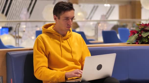 młody człowiek pracujący na laptopie w dużej nowoczesnej kawiarni  - Materiał filmowy, wideo