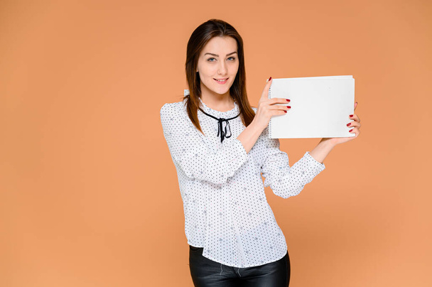 Secretary concept with a folder in hands. Portrait of a pretty woman in a white blouse with smooth dark hair. He stands in front of the camera, smiles, shows emotions on an orange background. - Photo, image