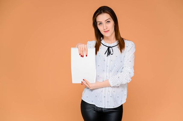 Secretary concept with a folder in hands. Portrait of a pretty woman in a white blouse with smooth dark hair. He stands in front of the camera, smiles, shows emotions on an orange background. - Foto, imagen