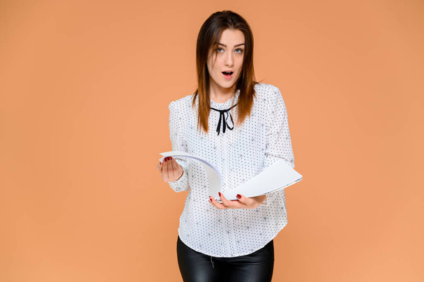 Secretary concept with a folder in hands. Portrait of a pretty woman in a white blouse with smooth dark hair. He stands in front of the camera, smiles, shows emotions on an orange background. - Fotoğraf, Görsel