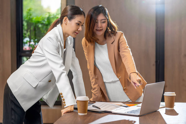 Zwei asiatische Geschäftsfrauen, die mit dem Partnerunternehmen per Technologie-Laptop im modernen Besprechungs-, Büro- oder Arbeitsraum arbeiten, Kaffeepause, Partner- und Kollegenkonzept - Foto, Bild