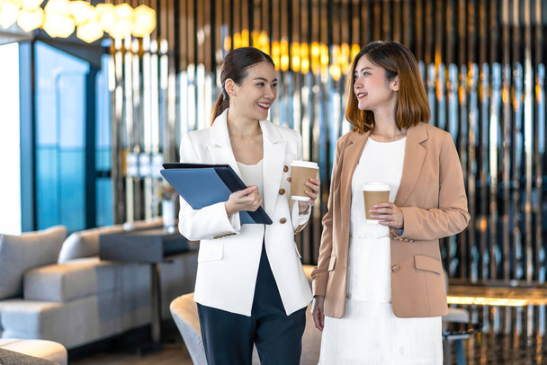 Two asian businesswomen talking during coffee break in modern office or coworking space, coffee break, relaxing and talking after working time, business and people partnership concept - Foto, afbeelding