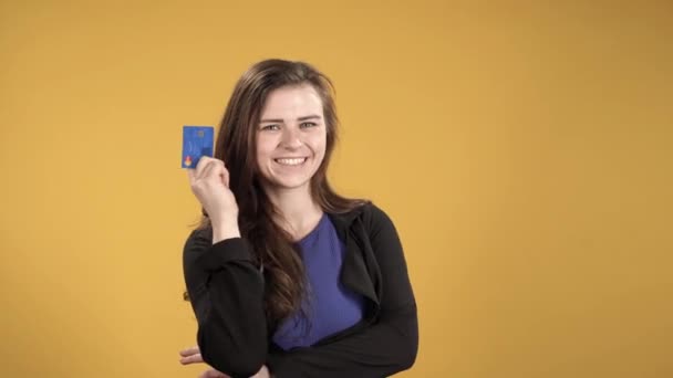 Happy woman holding credit card on yellow background - Filmagem, Vídeo