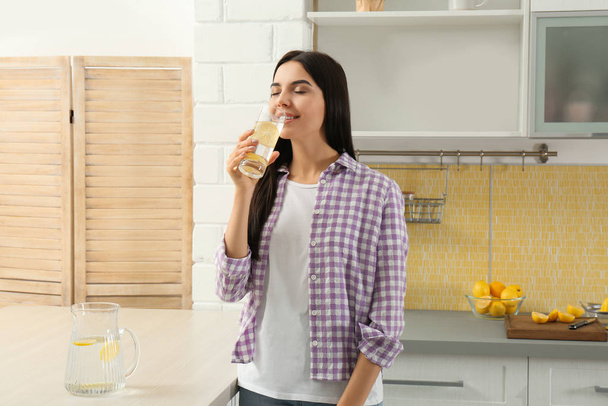 Beautiful young woman drinking lemon water in kitchen - Foto, imagen