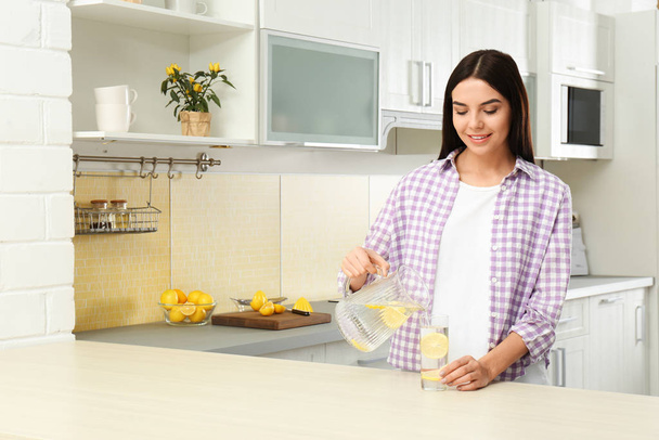 Beautiful woman pouring lemon water into glass from jug in kitch - Foto, Imagen