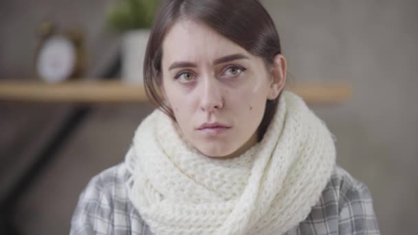 Portrait of sad Caucasian brunette girl in white scarf looking around. Pretty ill woman spending day at home. Healthcare, medicine, illness. - Materiał filmowy, wideo