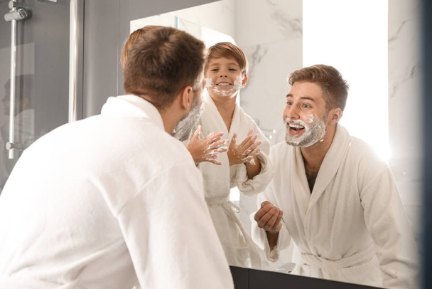 Dad and son with shaving foam on faces in bathroom - Photo, image