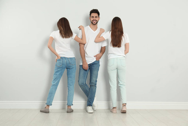 Skupina mladých lidí ve stylových džínách u světlé stěny - Fotografie, Obrázek