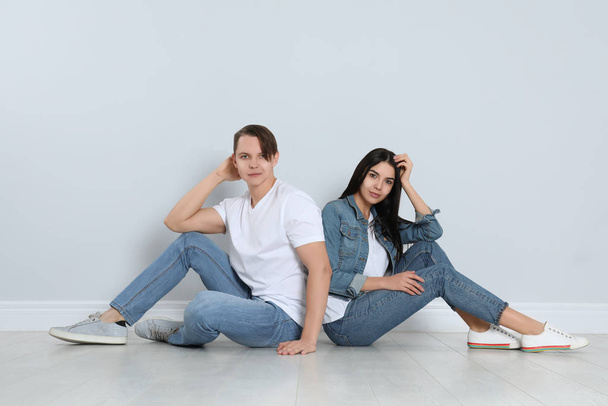 Young couple in stylish jeans sitting near light wall - Foto, afbeelding