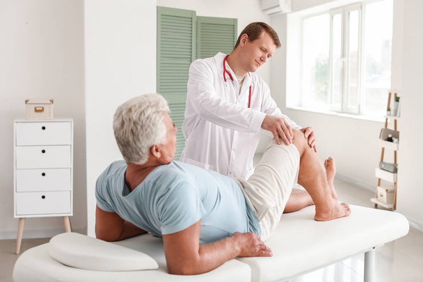 Врач осматривает зрелого мужчину с болью в суставах в клинике
 - Фото, изображение