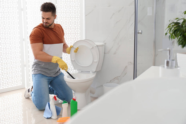 Young man feeling disgust while cleaning toilet bowl in bathroom - Φωτογραφία, εικόνα