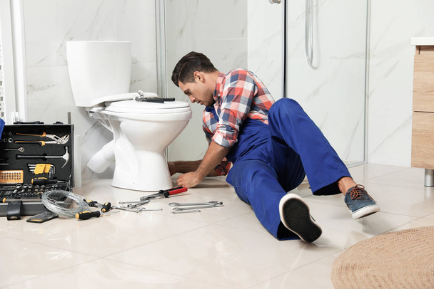 Professional plumber working with toilet bowl in bathroom - Фото, изображение