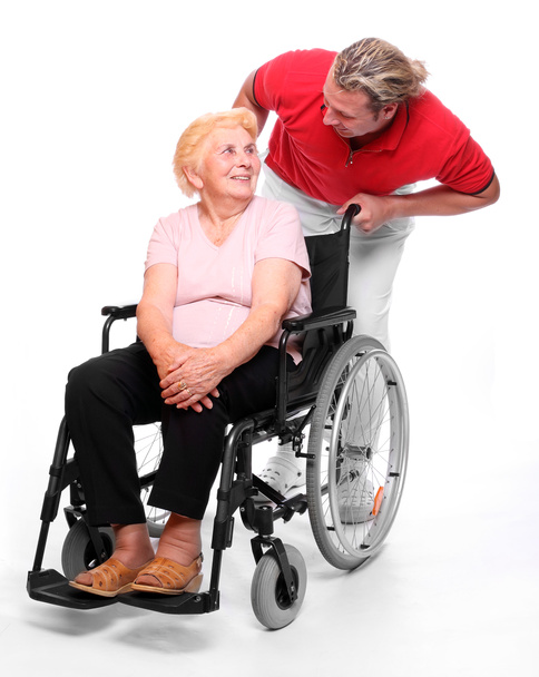 Пожилая парализованная женщина, сидящая в инвалидном кресле, и ее медбрат
 - Фото, изображение