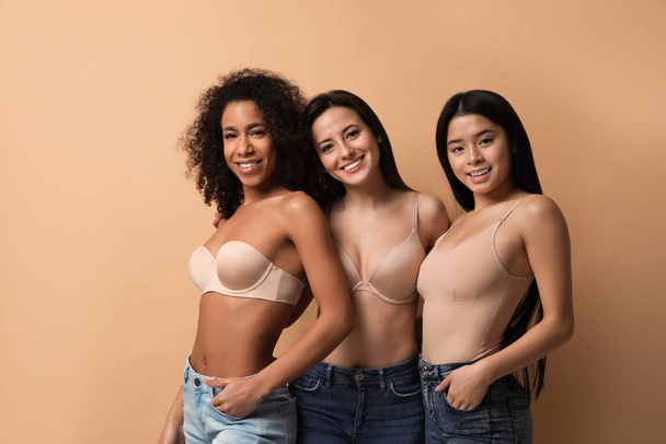 Group of women with different body types in jeans and underwear on beige background - Фото, зображення