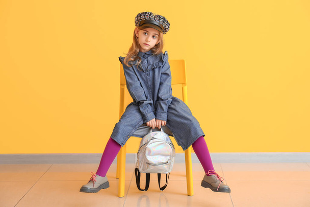 Cute little girl w jesieni ubrania siedzi w pobliżu ściany kolor - Zdjęcie, obraz