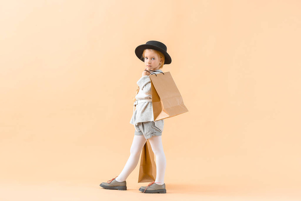 Cute little girl in autumn clothes and with shopping bags on light background - 写真・画像