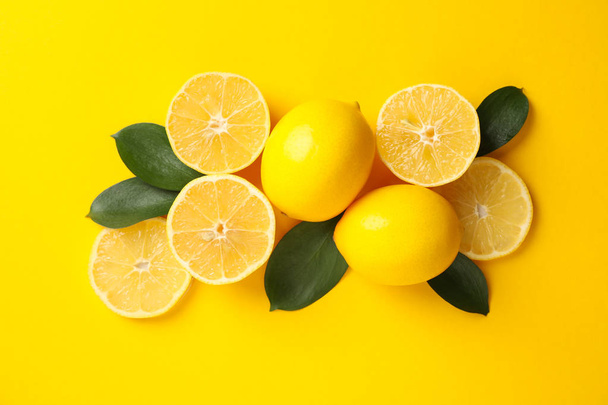Juicy lemons and leaves on yellow background, top view - Photo, Image