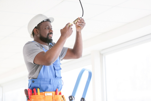 Electricista afroamericano realizando cableado en la habitación
 - Foto, Imagen