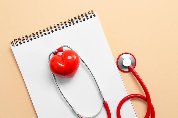 Stethoscope, σημειωματάριο και κόκκινη καρδιά σε φόντο χρώμα. Καρδιολογική έννοια - Φωτογραφία, εικόνα