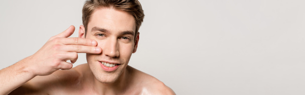 улыбающийся сексуальный мужчина с голым туловищем, касающимся чистого лица, изолированного на сером, панорамном снимке
 - Фото, изображение