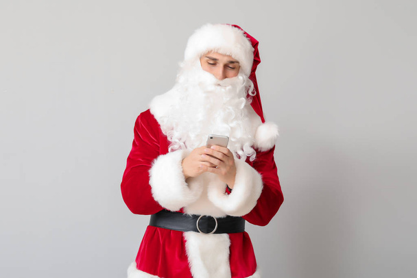 Young man in Santa costume and with mobile phone on light background - Photo, Image