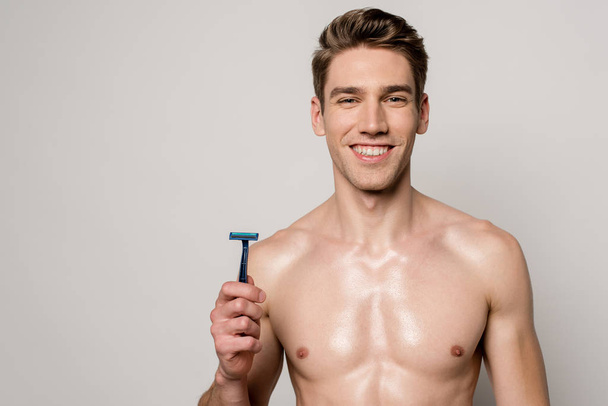 smiling sexy man with muscular torso holding shaver isolated on grey - Фото, изображение