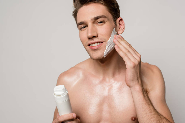 sonriente sexy hombre con torso muscular aplicación de espuma de afeitar aislado en gris
 - Foto, Imagen