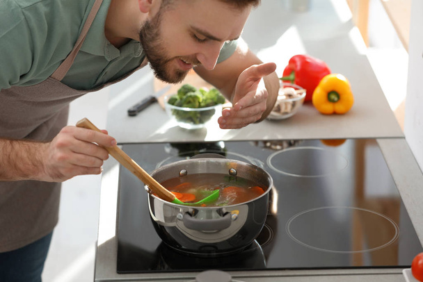 Young man cooking delicious soup in kitchen - Photo, Image