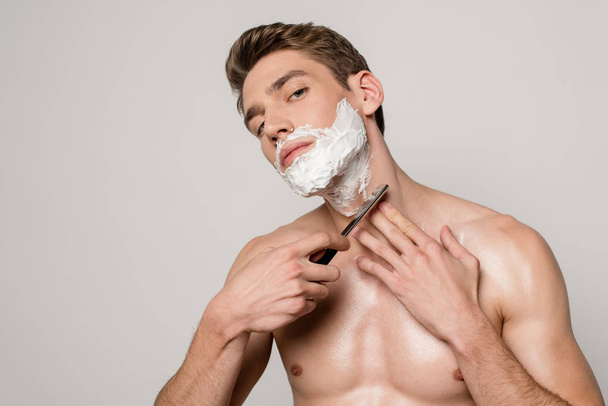 sexy man with muscular torso shaving with straight razor isolated on grey - Zdjęcie, obraz