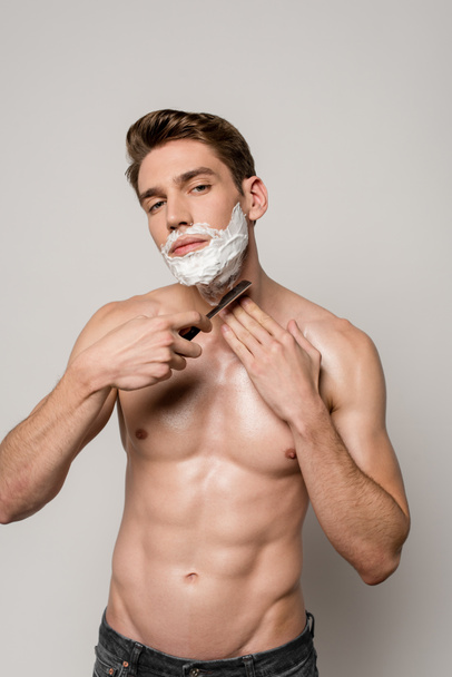 сексуальный мужчина с мышечным туловищем бритья с прямой бритвой изолированы на сером
 - Фото, изображение