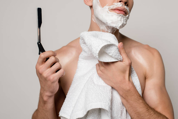 levágott kilátás szexi férfi izmos törzs és borotválkozás hab az arcon gazdaság egyenes borotva és törölköző elszigetelt szürke - Fotó, kép