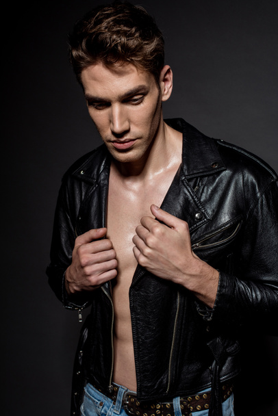 sexy young man with muscular torso in biker jacket and jeans on black background - 写真・画像